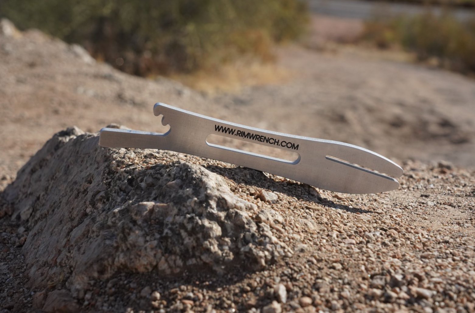 RimWrench aluminum bicycle rim dent repair tool resting on a desert rock