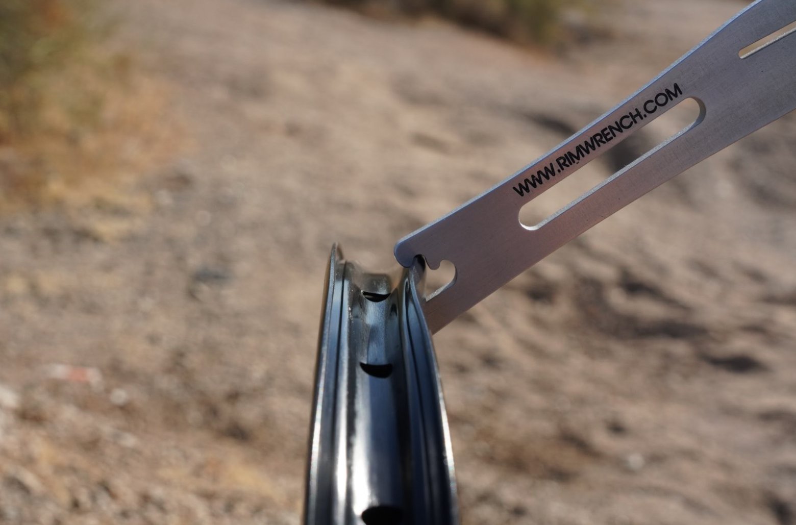 RimWrench hooked onto a dented aluminum bicycle rim showing the repair technique